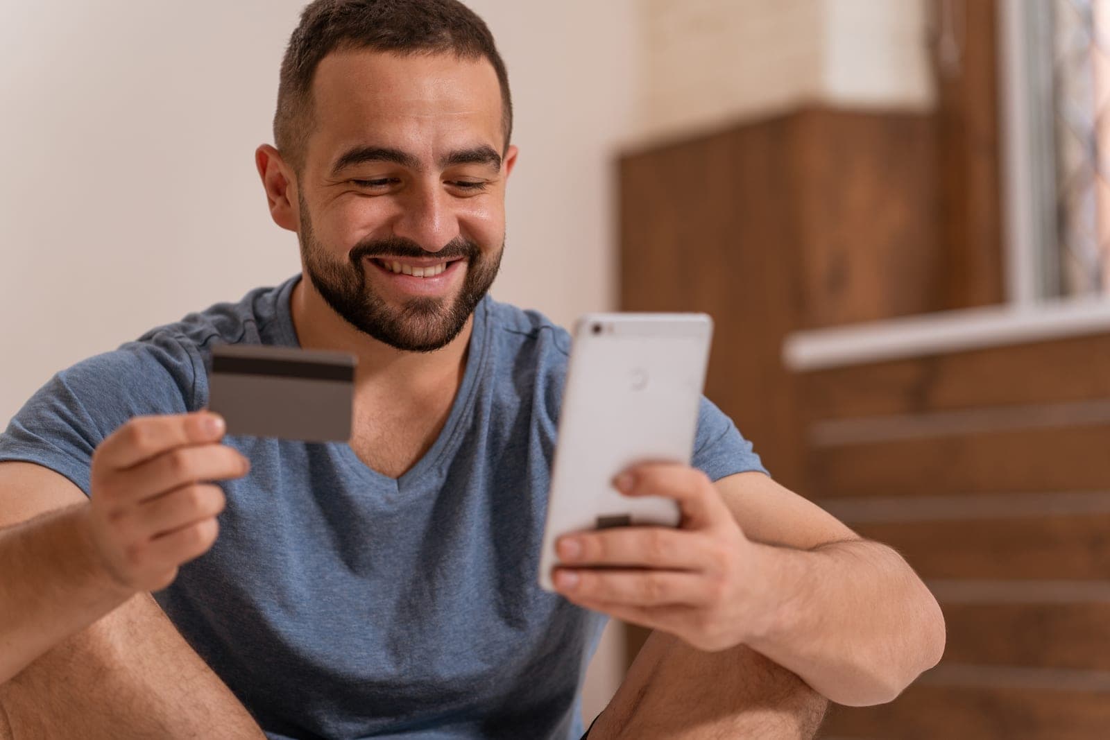 A smiling man holding a credit card and a phone