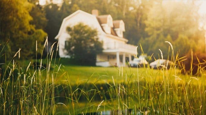 A white farmhouse beyond a field of tall grass at sunset